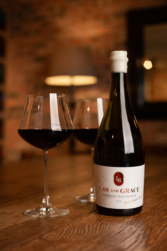 Wine bottle with 'Law and Grace' label next to two filled wine glasses on a wooden table.